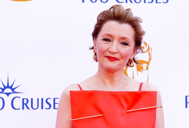 Lesley Manville smiling while posing for photos at a red carpet event