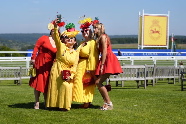 Racegoers in red and yellow dresses take photographs during day one of the Qatar Goodwood Festival at the Goodwood Racecourse, Chichester