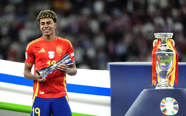 Spain's Lamine Yamal stands smiling alongside the European Championship trophy after beating England in Berlin. 