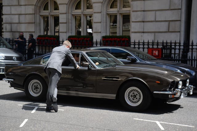 A stunt double stands beside an Aston Martin