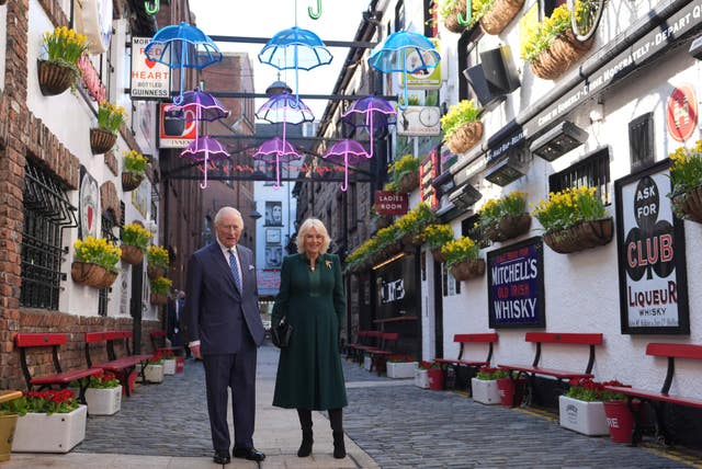 Charles and Camilla standing underneath illuminated umbrellas on Commercial Court in Belfast