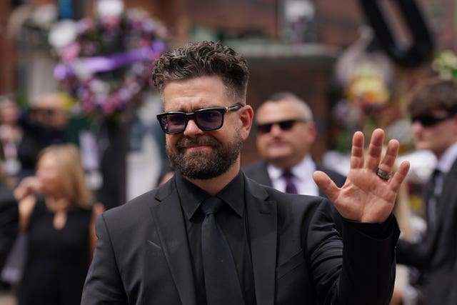 Jack Osbourne waves to the crowd after viewing the messages and floral tributes left at the Black Sabbath Bridge bench on Broad Street in Birmingham