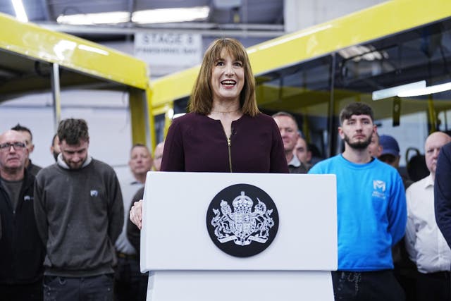 Rachel Reeves smiling while speaking from a podium in a factory, with workers behind her