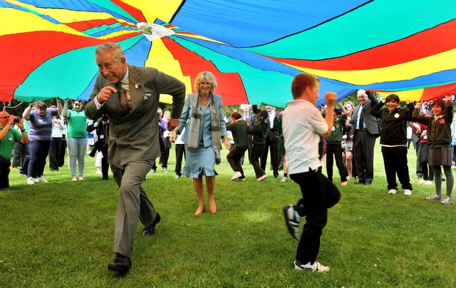 The Prince of Wales and the Duchess of Cornwall run under a brightly coloured Parachute during a youth rally on their last visit to Guernsey in 2012