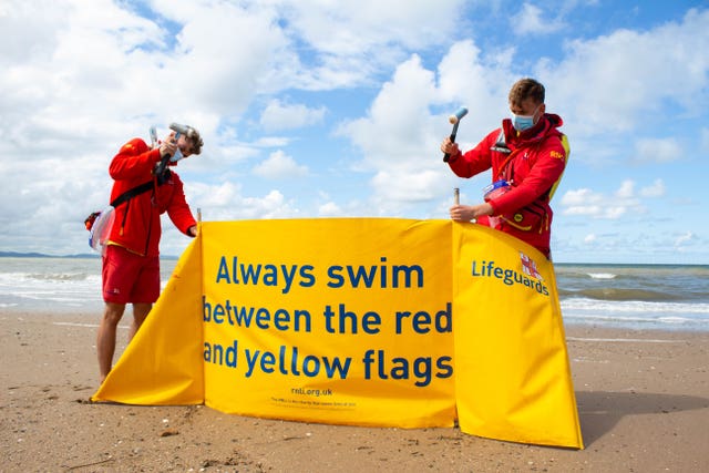 Two lifeguards install a banner about swimming safety precautions
