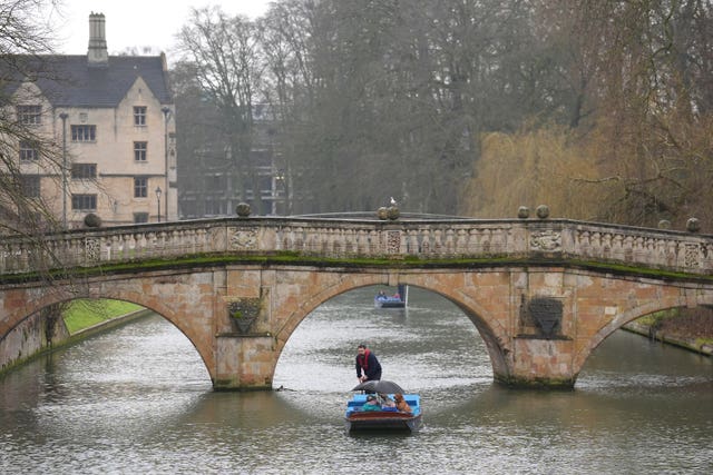 People shelter from the rain under umbrellas as they punt along the River Cam in Cambridge.