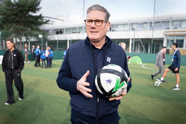 Labour leader Keir Starmer stands on astroturf holding a white and black football