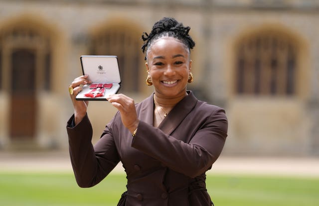 Sadia Kabeya smiling while holding up her MBE medal
