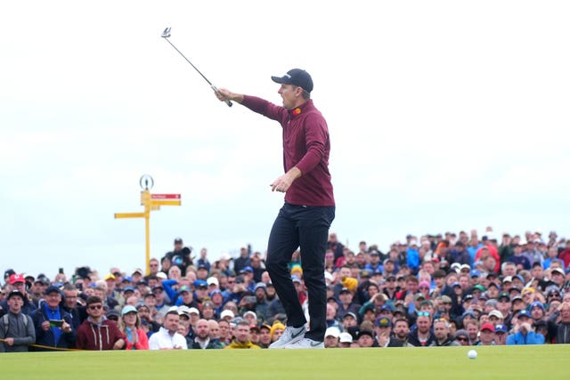 Justin Rose raises his putter in the air in front of a packed gallery