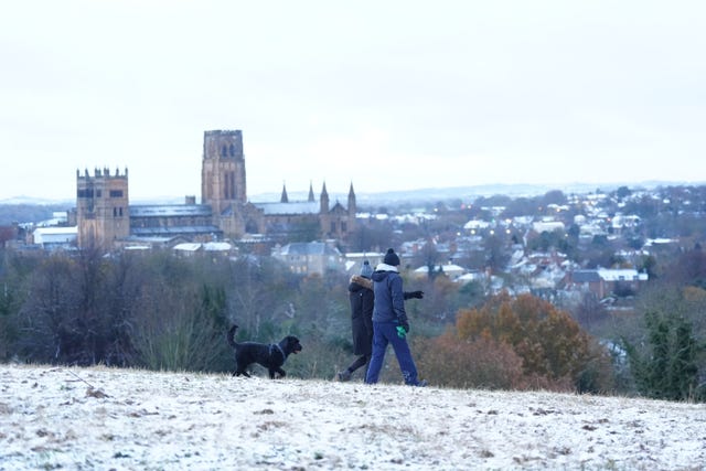 People walk a dog on snow covered hill near to Durham Cathedral