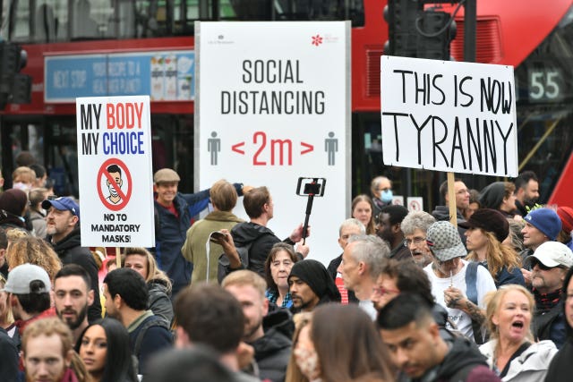 Protesters during an anti-lockdown rally pass a social distancing sign on Tottenham Court Road, London (Dominic Lipinski/PA)