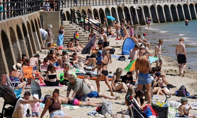 A crowded stretch of sand between a concrete wall and the sea 