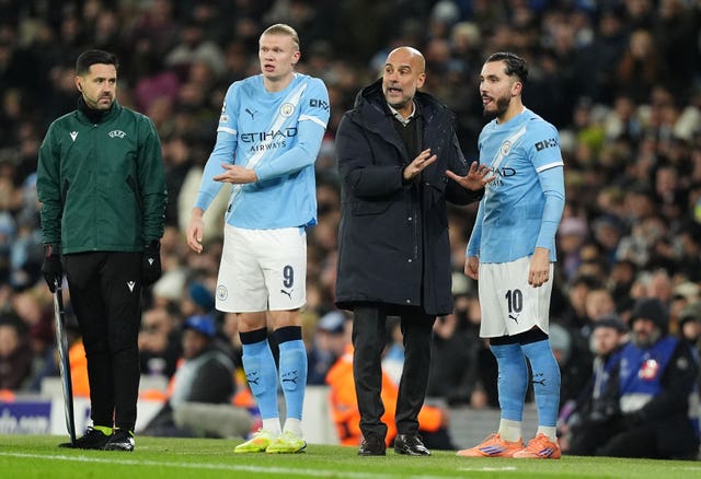 Manchester City substitutes Erling Haaland (centre left) and Rayan Cherki (right) wait to enter the pitch with manager Pep Guardiola 