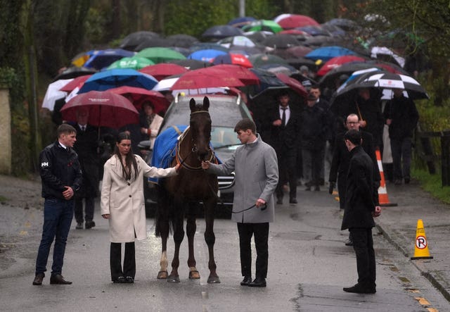 The hearse carrying the coffin of Michael O’Sullivan is led by the racehorse Barr Na Sraide away from the grounds following the funeral at St John the Baptist Church, Glantane