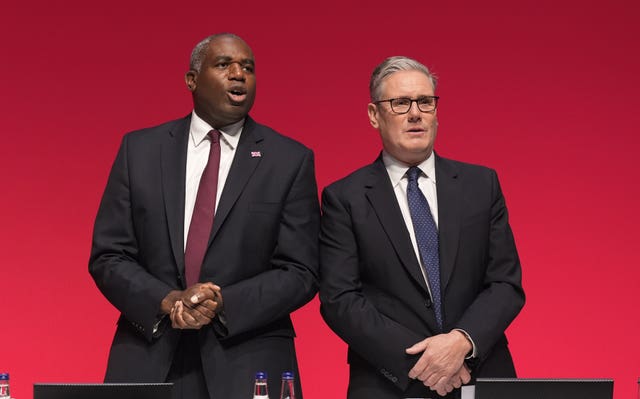 David Lammy, left, and Sir Keir Starmer wearing suits standing in front of a red background