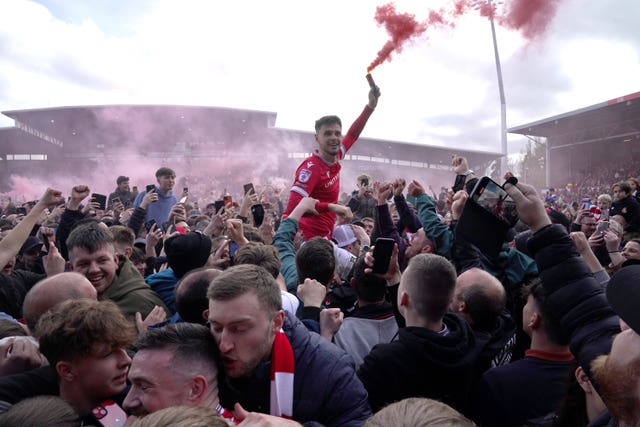 A football fan with a flare is hoisted aloft at Wrexham's football stadium 