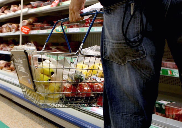 A man holding a shopping basket full of food in a supermarket