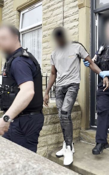 Still from a video of a man being led out of a house by a police officer