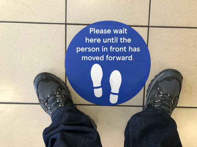 Social distancing signage on the floor of a Tesco petrol station in Glasgow asking for customers to wait until the person in front has moved forward.