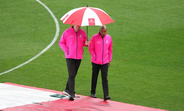 Umpires Chris Brown, left,  and Joel Wilson shelter under an umbrella while inspecting the outfield