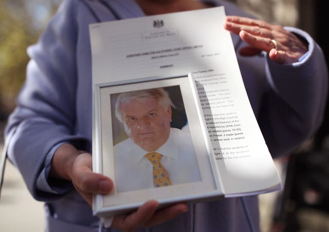 Karen Wilson, widow of postmaster Julian Wilson who died in 2016, holds his picture outside an earlier hearing