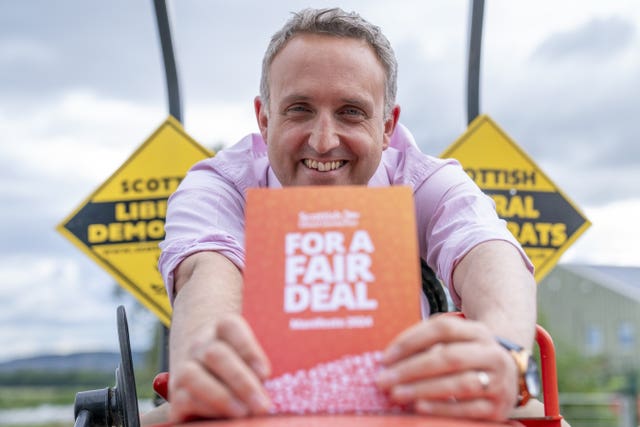 Alex Cole-Hamilton smiling as he holds a copy of the Lib Dem manifesto