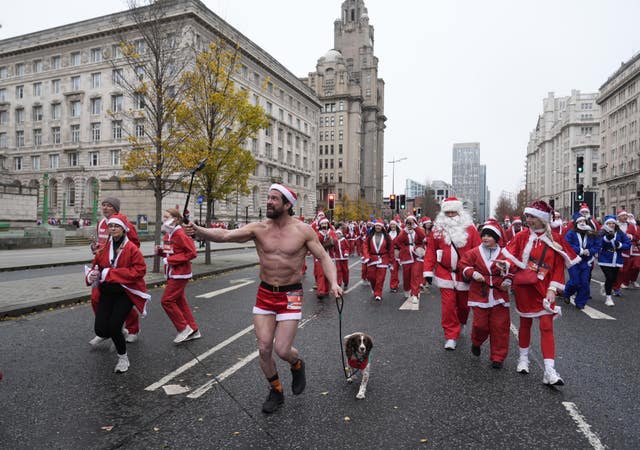 A shirtless Santa runs with a dog in front of a crowd 