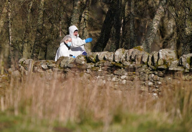 Police officer in white forensic suit behind a dyke in a rural area