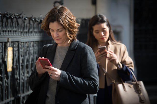 Two women check their mobile phones in central London (Stefan Rousseau/PA)