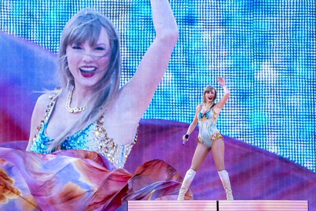 Taylor Swift smiling and waving to fans while performing in a blue and gold sparkly bodysuit