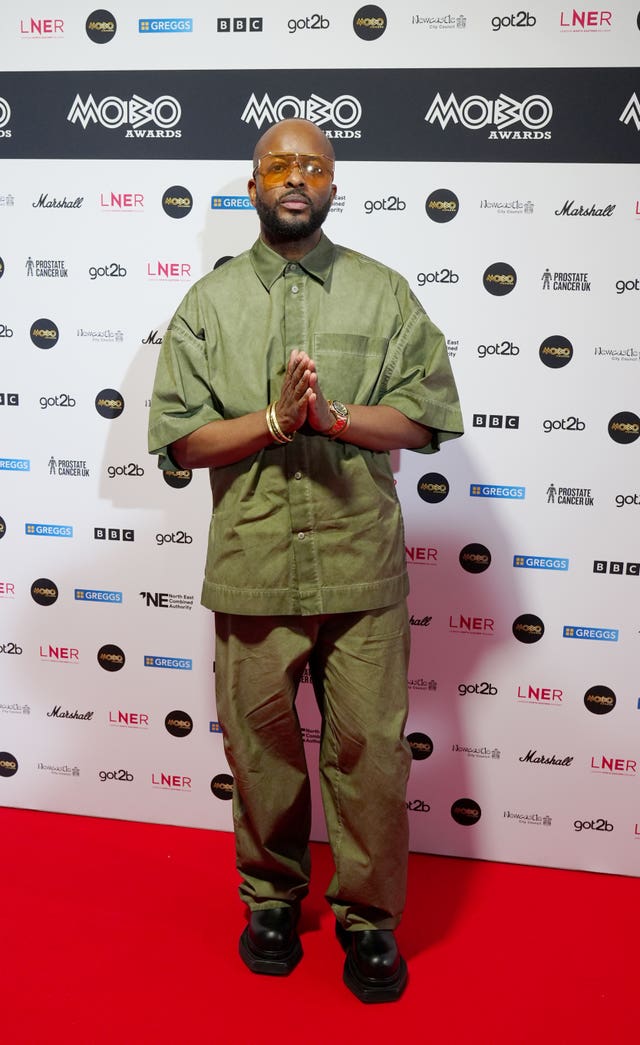 Manny Norte dressed in green and holding his hands out in front of him in a praying motion on the red carpet