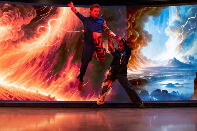 Two men dancing in front of red and blue imagery inside a studio