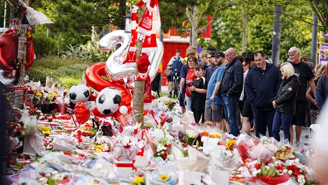 People standing by floral tributes and balloons