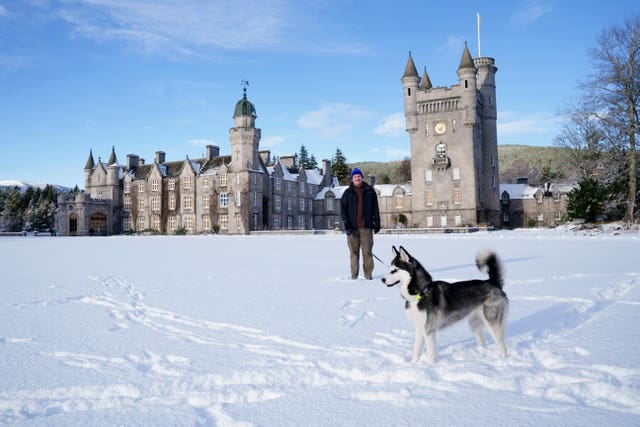 A man smiles while walking his Siberian husky in the snow outside Balmoral Castle