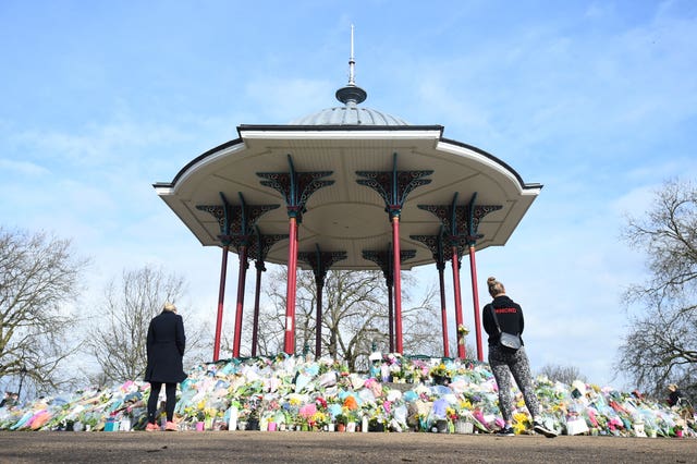 People stand next to floral tributes left at the band stand in Clapham Common for Sarah Everard