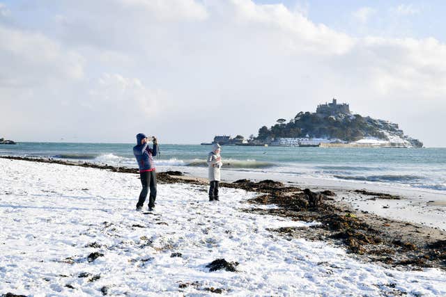 People stand on the snow-covered Marazion beach, with St Michael’s Mount in the background, in Cornwall, (Ben Birchall/PA)