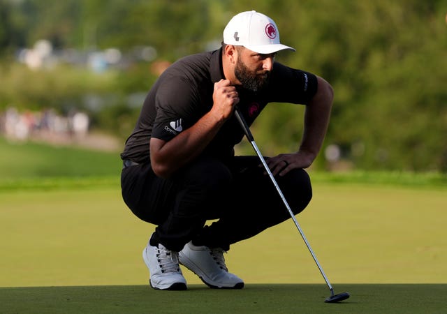 Jon Rahm crouches down to read a putt