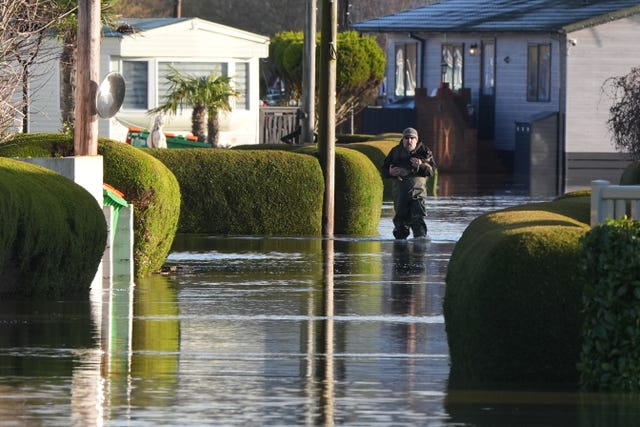 A man wearing waders carries a dog at The Little Venice caravan park in Yalding, Kent