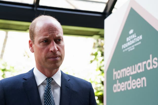 William, the Prince of Wales, stands next to a sign for his homelessness project Homewards