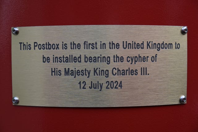 The plaque with wording announcing the postbox is the first in the UK with the King's cypher