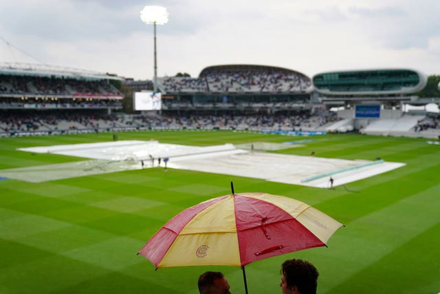 Spectators put up umbrellas as rain stops play during day one at Lord's