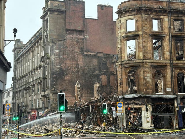 A collapsed building, which shows signs of fire damage and is having water sprayed on it