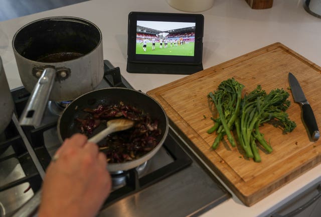 A fan watches the Aston Villa v Sheffield United Premier League match on an iPad as they cook dinner 