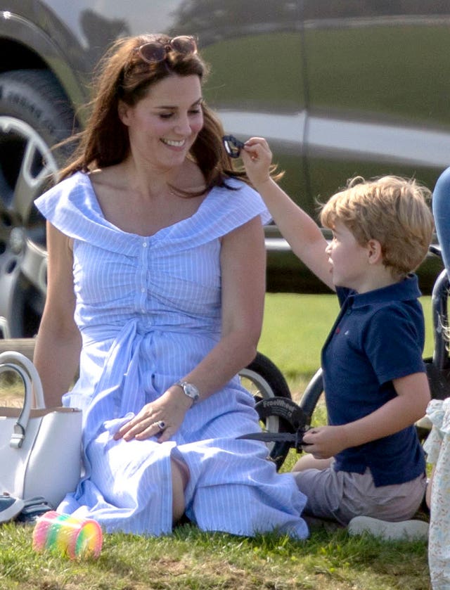 Prince George plays with a toy knife as he sits with his mother the Duchess of Cambridge