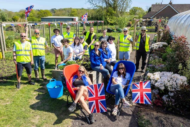 People, some wearing hi-vis, some holding spades and some waving Union flags, raise their hands in the air at a garden created at the Veterans' Growth centre near Battle, East Sussex