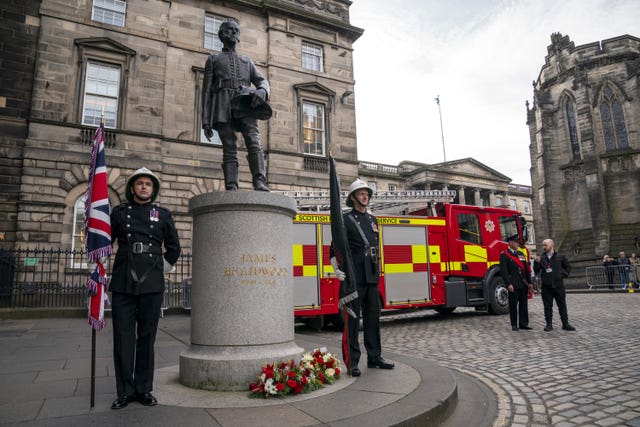 Statue of James Braidwood flanked by fire officers with a fire engine in the background