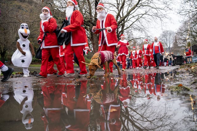 People dressed as Santa walk past a puddle with a dog 