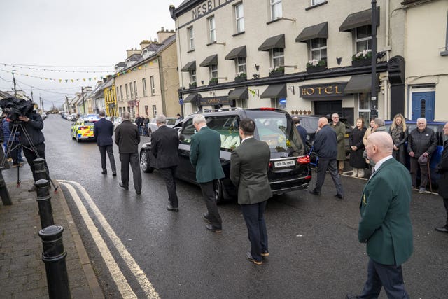 The funeral cortege arrives ahead of the service at the Church Of The Holy Family