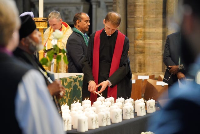A member of the clergy lights candles with the names of the victims on them during the Grenfell fire memorial service at Westminster Abbey in London