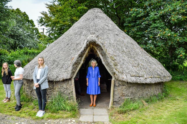 The Duchess of Cornwall peers out from a traditional straw hut during a visit to the Youth Action Wiltshire Oxenwood Outdoor Activity Centre near Marlborough, Wiltshire 